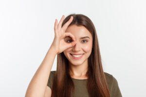 Ragazza sorridente che unisce pollice e indice davanti all'occhio destro