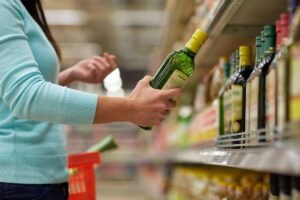 Donna al supermercato con una bottiglia di olio extravergine d'oliva in mano