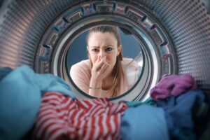ragazza si tappa il naso con il cestello della lavatrice aperto