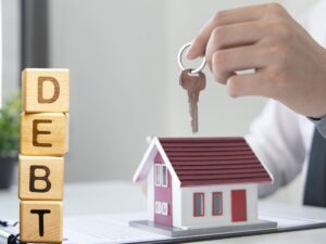 modellino di casa e persona che sorregge chiavi con scritta "debiti"